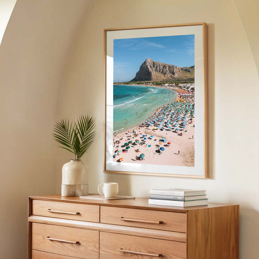 print of San Vito Lo Capo beach in Sicily with colourful umbrellas, turquoise water and Mount Monaco behind the bay.