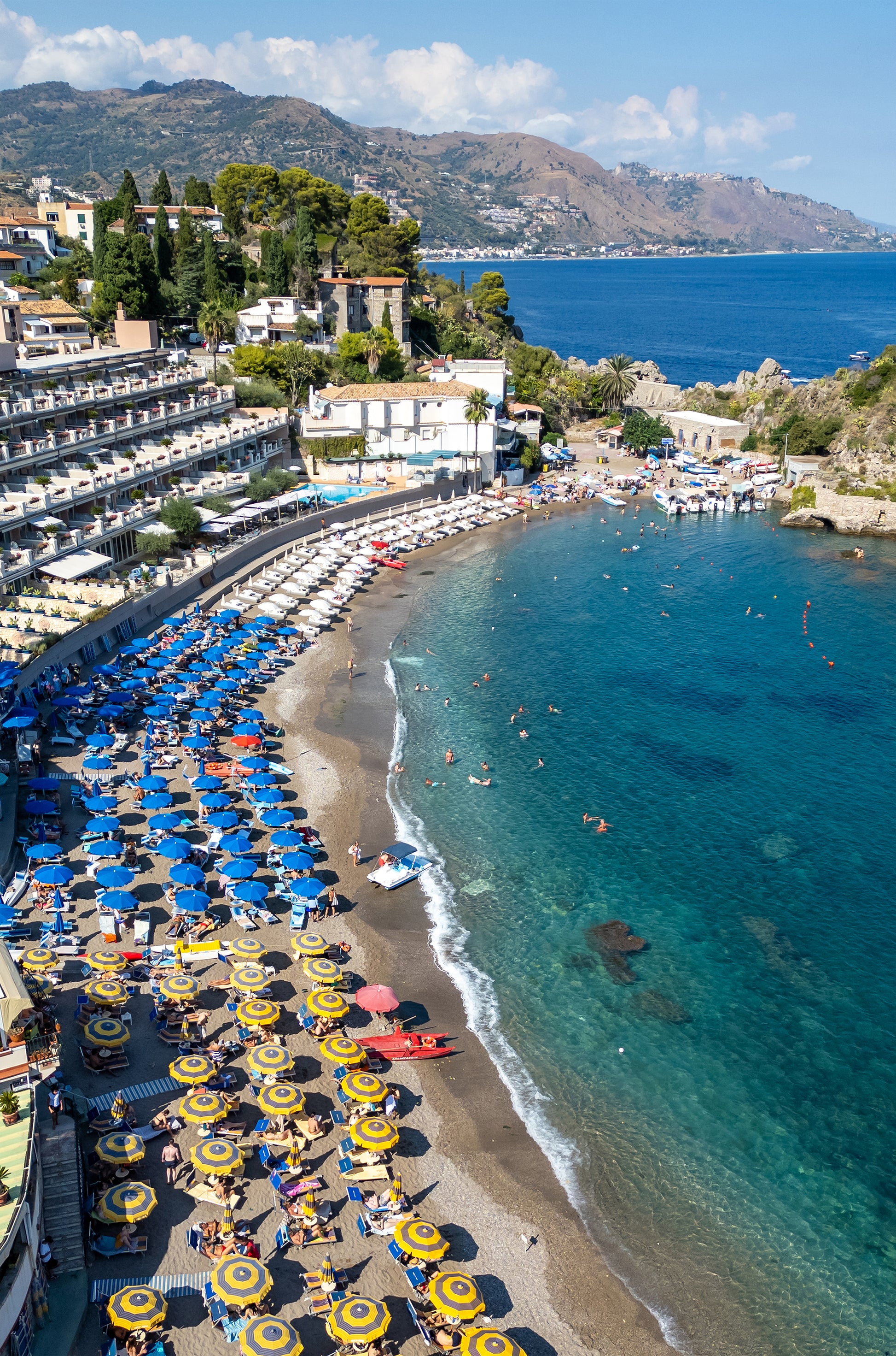 Aerial beach photo of Spiaggia di Mazzarò in Sicily showing turquoise water, golden sand, and rows of colourful umbrellas.