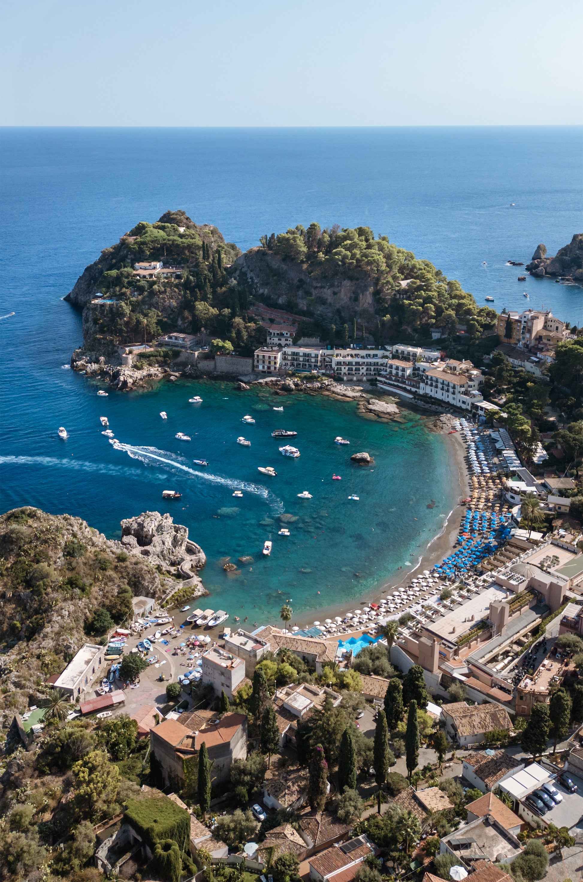 Portrait aerial photo of Spiaggia di Mazzarò in Sicily, showing deep blue Mediterranean water and beach from an inland viewpoint.