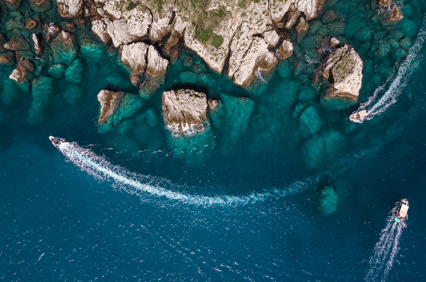 Bird’s eye aerial view of Taormina’s rocky coastline with a gradient into clear blue Mediterranean water.