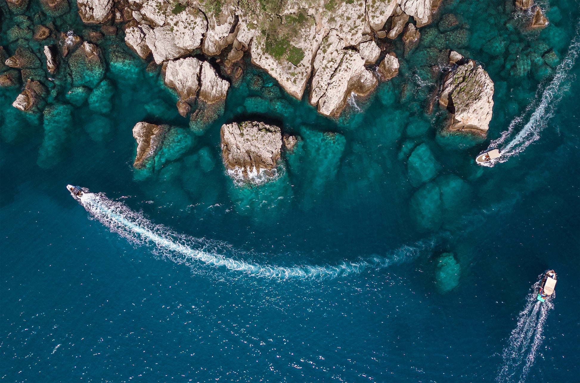 Bird’s eye aerial view of Taormina’s rocky coastline with a gradient into clear blue Mediterranean water.