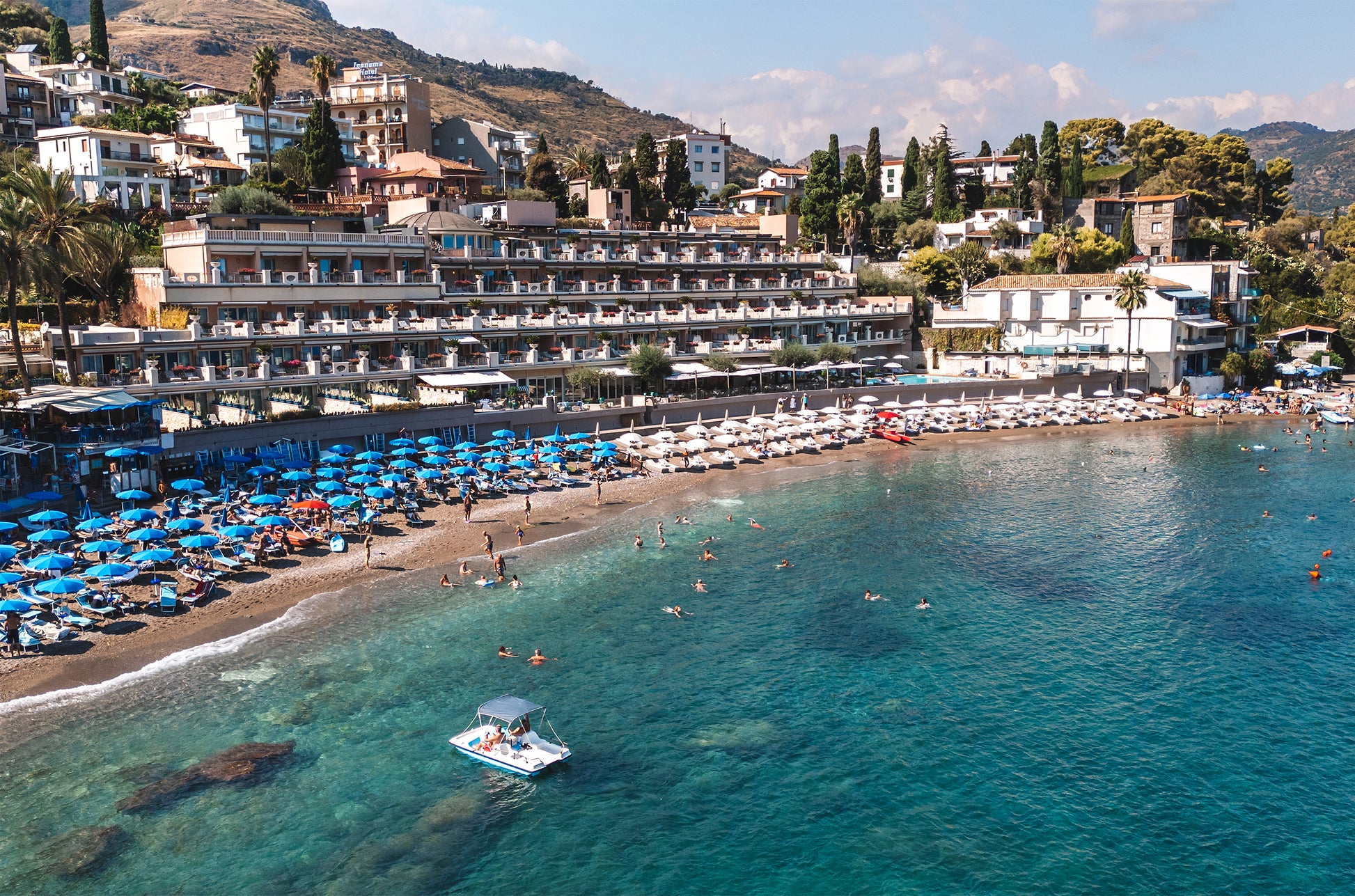 Aerial photo of Spiaggia Beach in Sicily with rows of beach umbrellas and a coastal resort along the shoreline.
