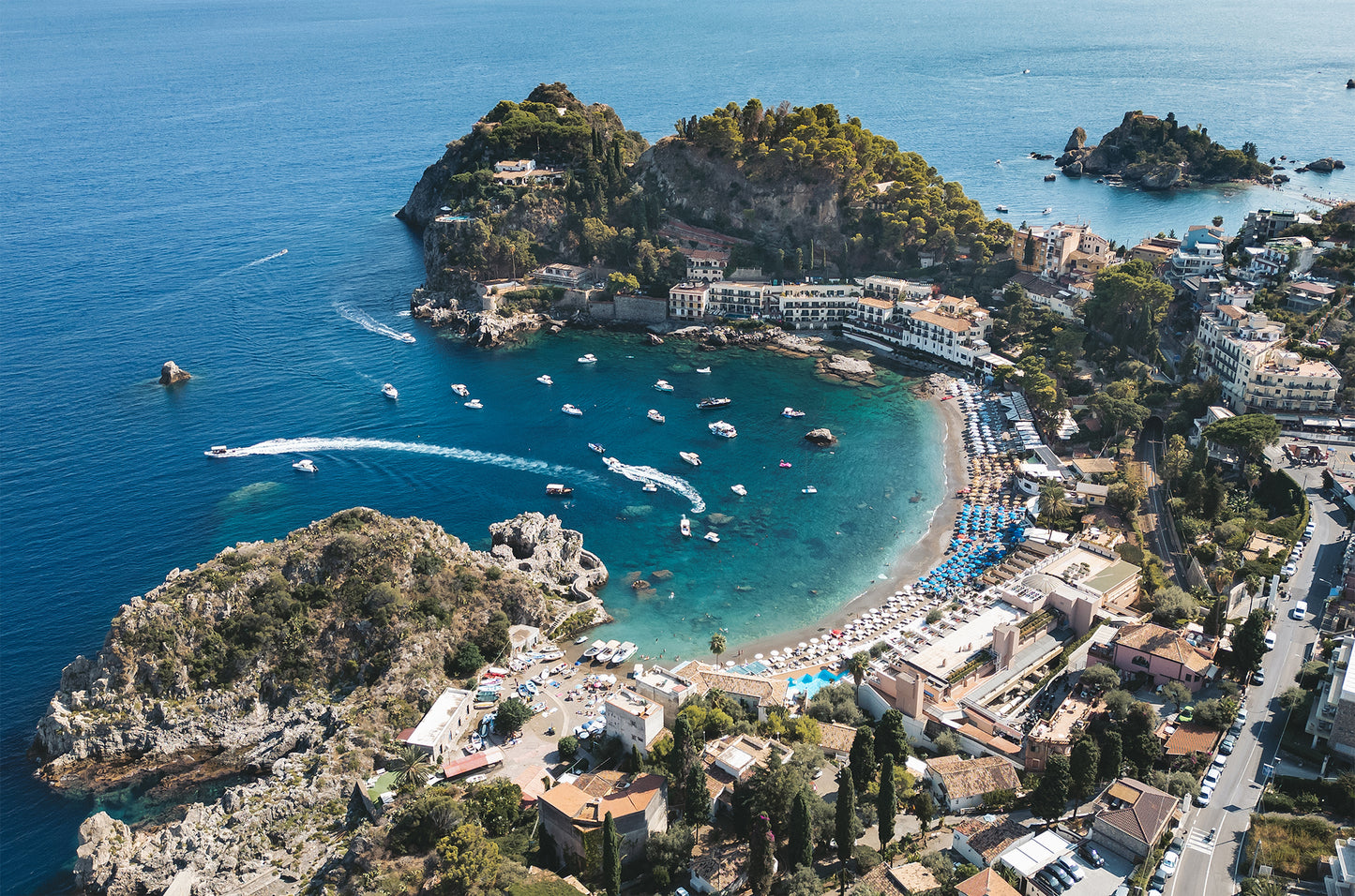 Landscape aerial photo of Spiaggia di Mazzarò in Sicily, with turquoise sea, sandy beach, and boats seen from an inland perspective.