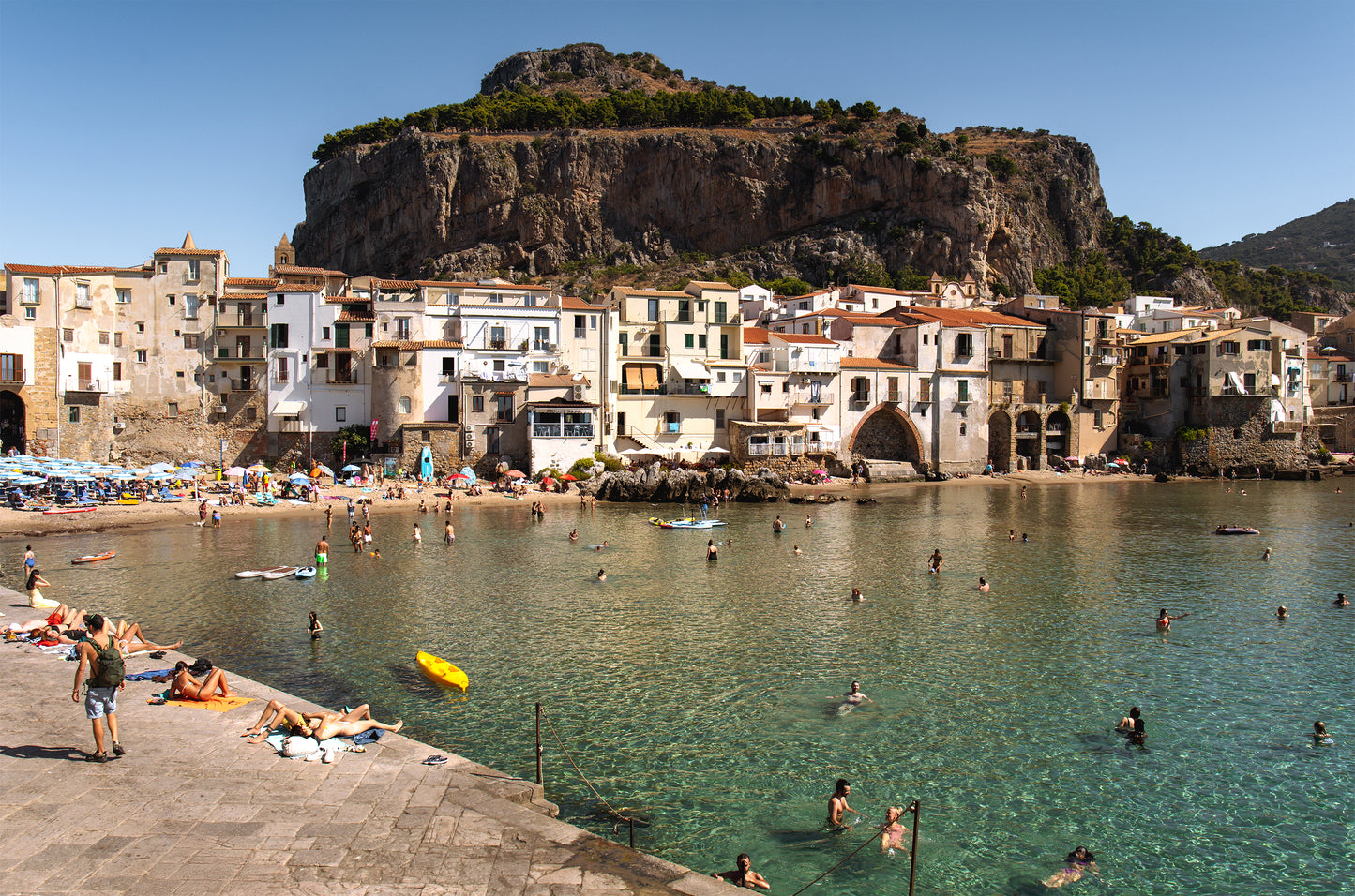The Old Town Shoreline, Cefalù wide coastal photography print taken from the jetty in Cefalù, Sicily, looking back toward historic buildings and the shoreline below.