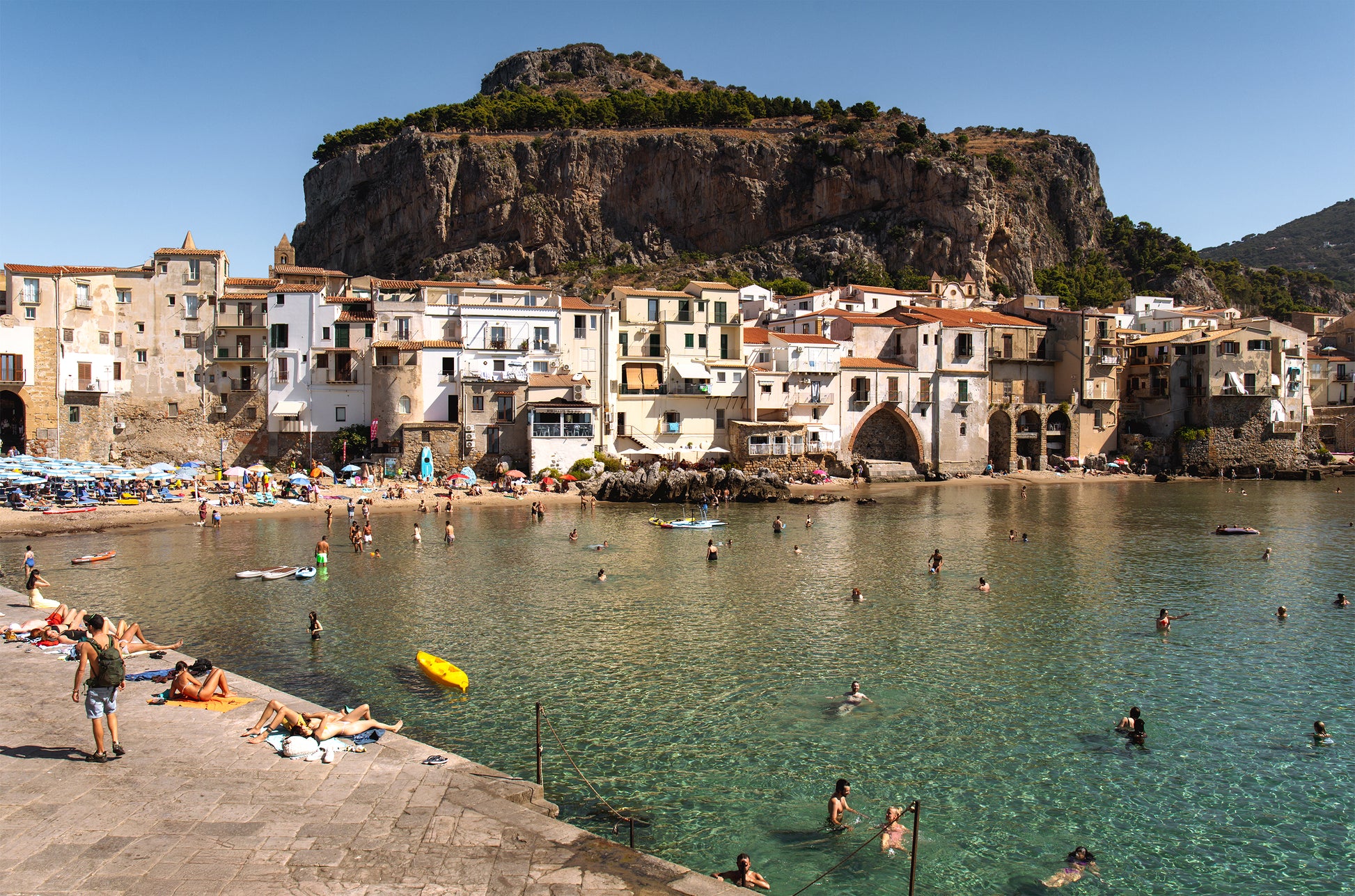 The Old Town Shoreline, Cefalù wide coastal photography print taken from the jetty in Cefalù, Sicily, looking back toward historic buildings and the shoreline below.
