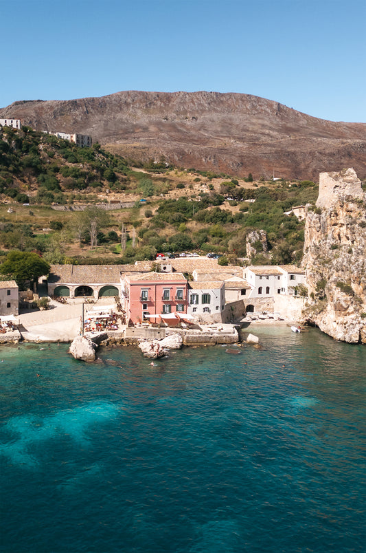 Drone photo of Scopello, Sicily looking down on the coastal town with a pink hotel and blue water