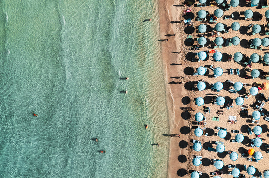 Overhead photo of San Vito Lo Capo beach in Sicily with turquoise ocean and colourful umbrellas on the sand.