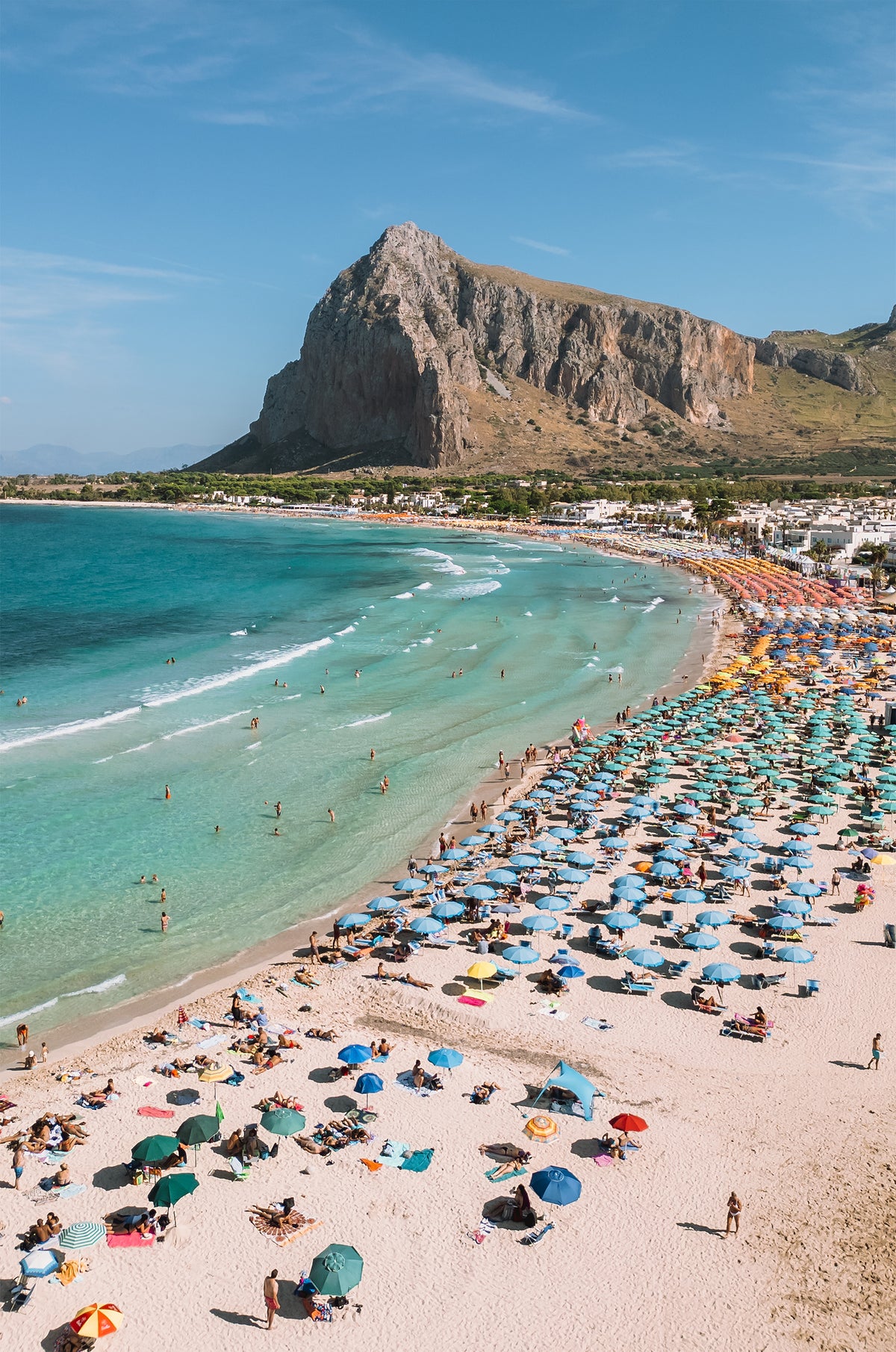 Photo of San Vito Lo Capo beach in Sicily with colourful umbrellas, turquoise water and Mount Monaco behind the bay.
