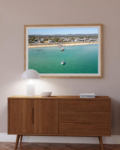 Safety Beach pier aerial print in a natural oak frame styled above a sideboard