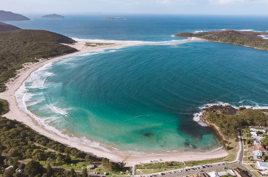 Aerial view of Fingal Bay near Port Stephens NSW, showing the curved beach, turquoise water and the Fingal Spit reaching toward forested headlands.
