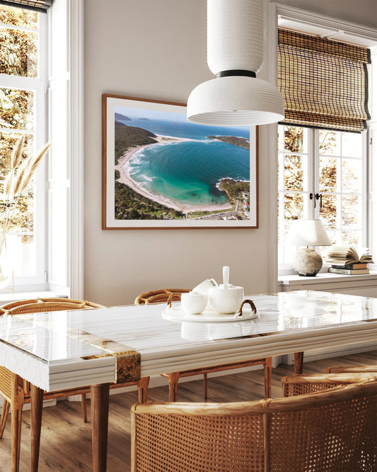 Fingal Bay aerial coastal print in a natural timber frame, styled above a marble dining table in a bright coastal room.