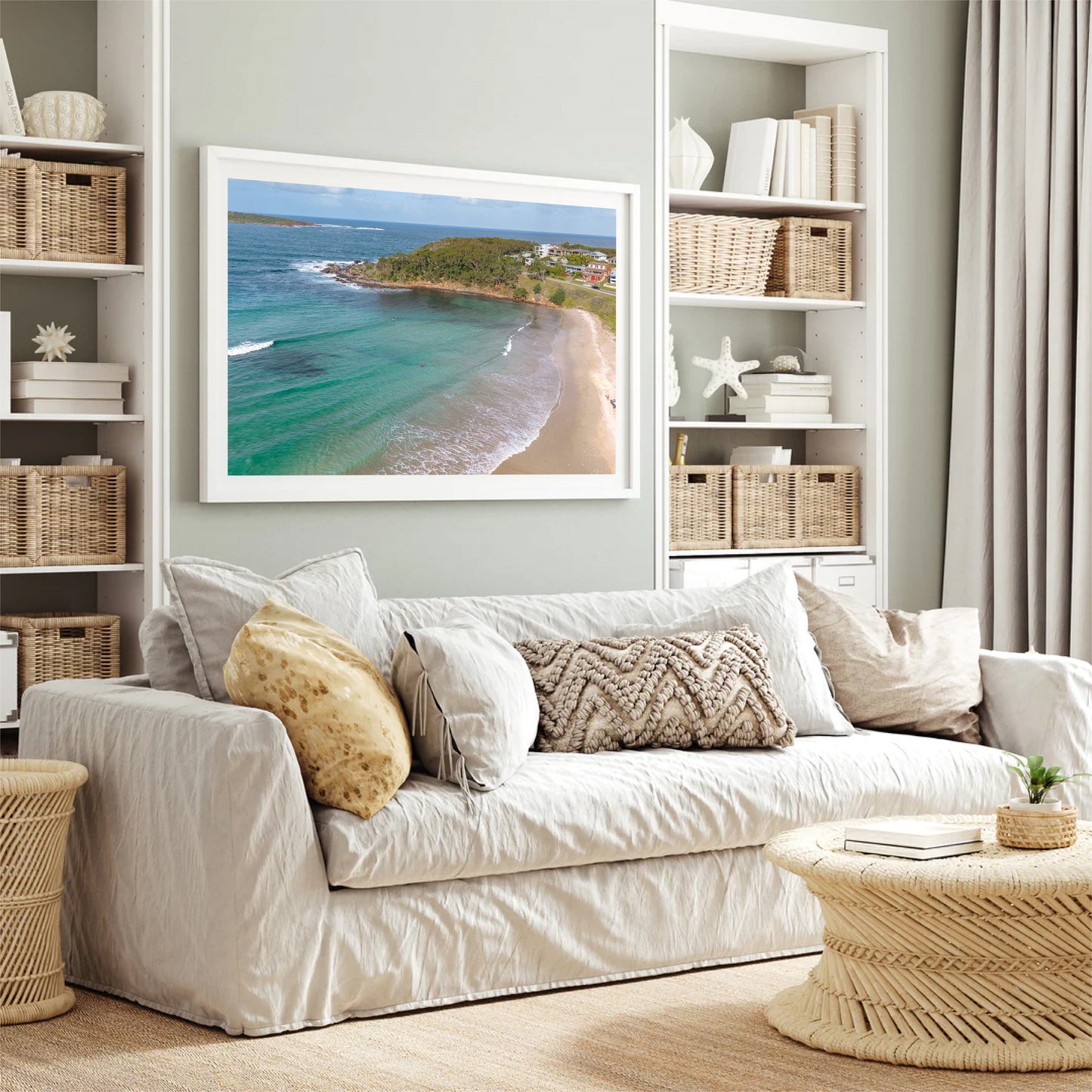 Fingal Bay cove print in a white frame, styled above a white sofa in a bright coastal living room with rattan baskets.