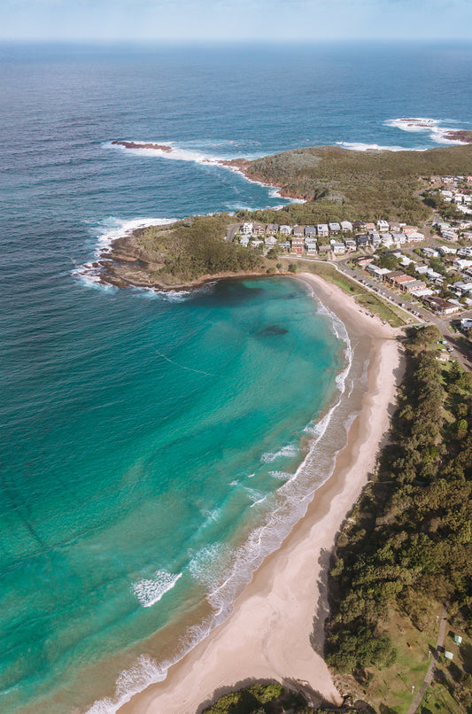 Portrait aerial of Fingal Bay near Port Stephens NSW, showing turquoise water curving around a headland cove and a long stretch of golden beach.