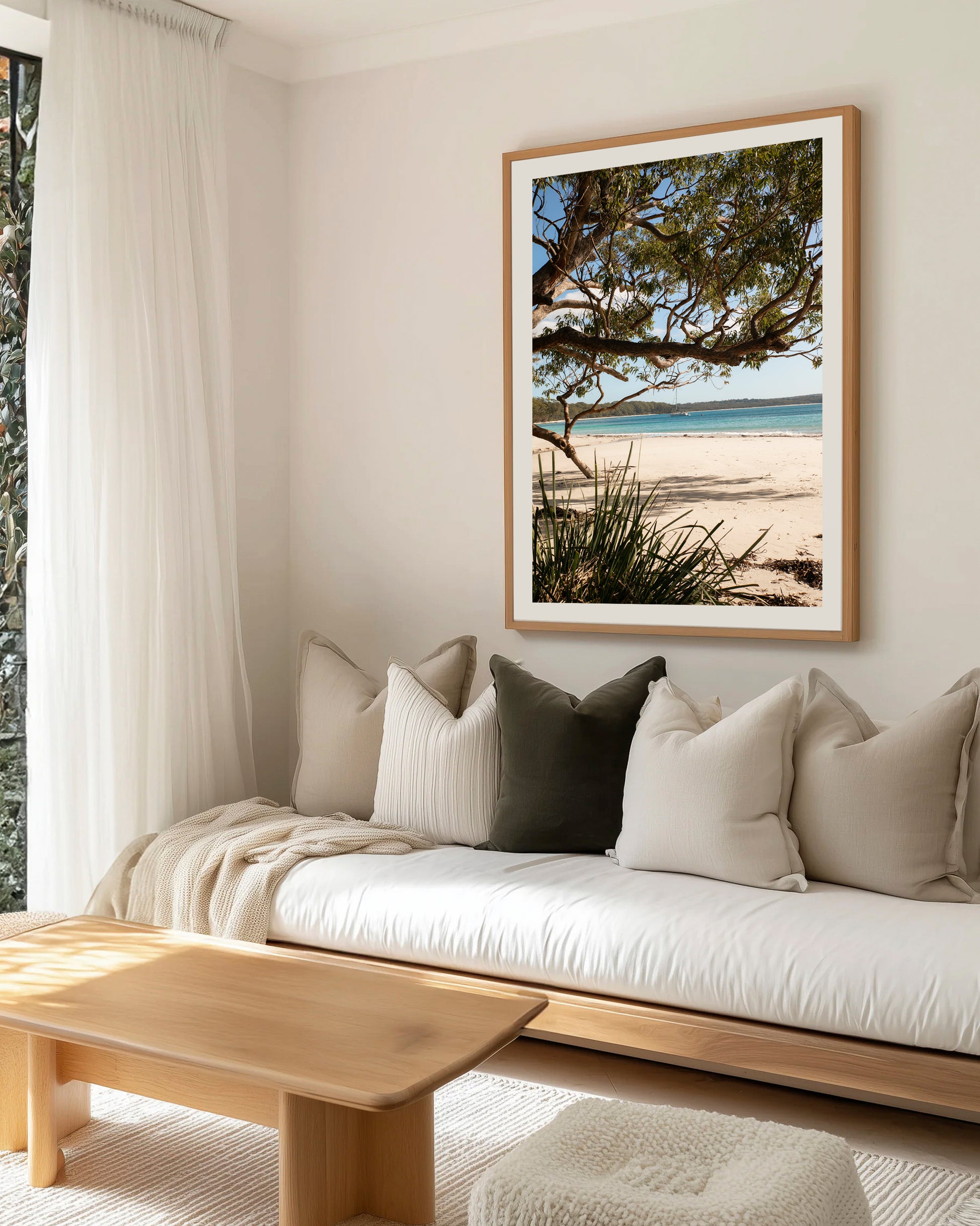Under the Gums Jervis Bay print in a natural oak frame, styled above a white daybed with linen cushions in a coastal lounge.
