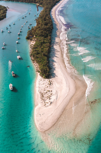 Portrait aerial of the Myola sand spit at Jervis Bay NSW, with yachts moored on Currambene Creek on one side and surf rolling onto Kite Beach on the other.