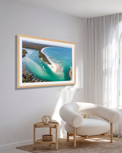 Myola Kite Beach wide print in a natural oak frame, styled above a side table in a bright reading corner with a boucle armchair.