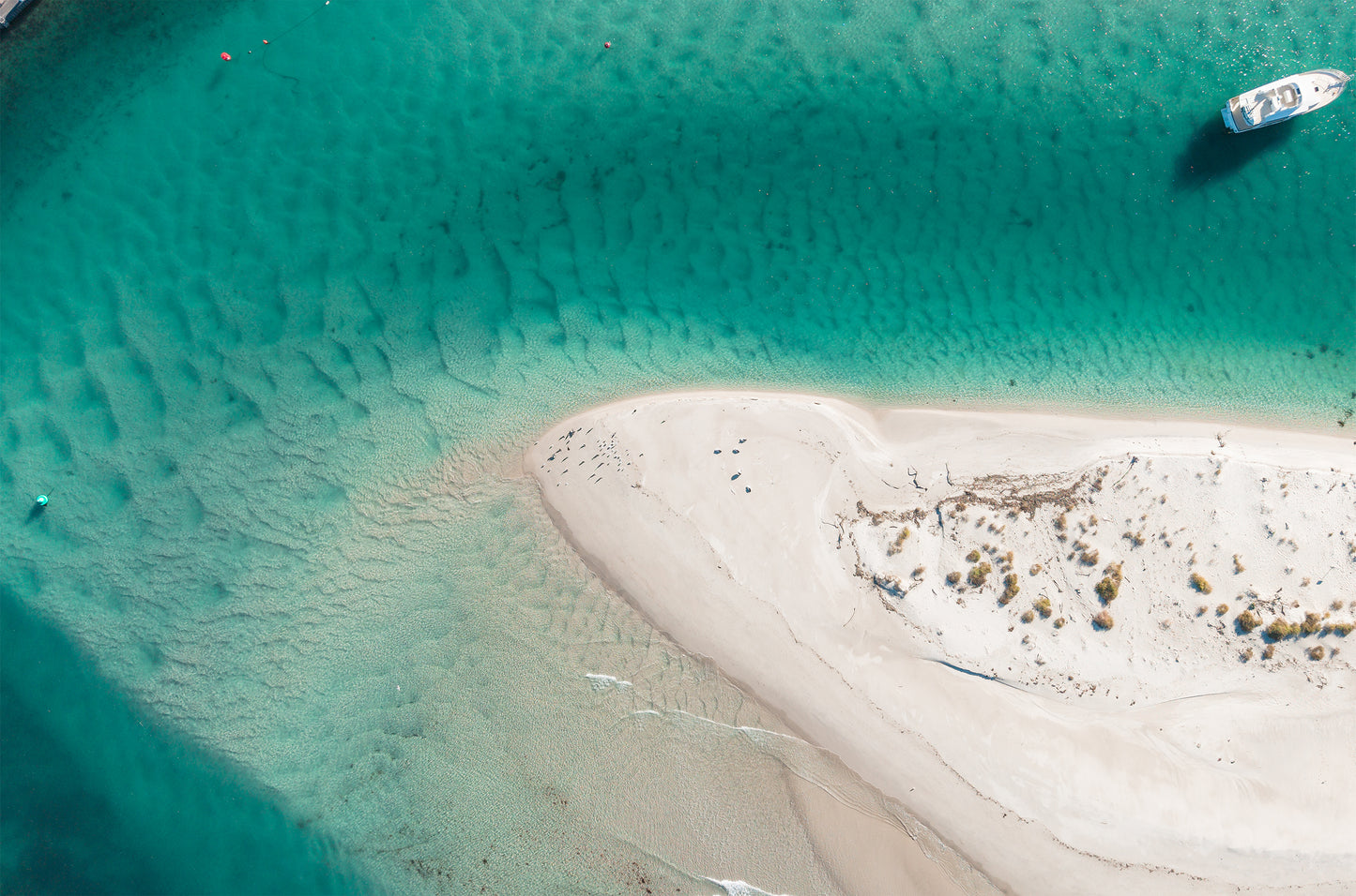 Top-down aerial of the white sand tip of Myola Point at Jervis Bay NSW, surrounded by rippled turquoise water with a boat nearby.