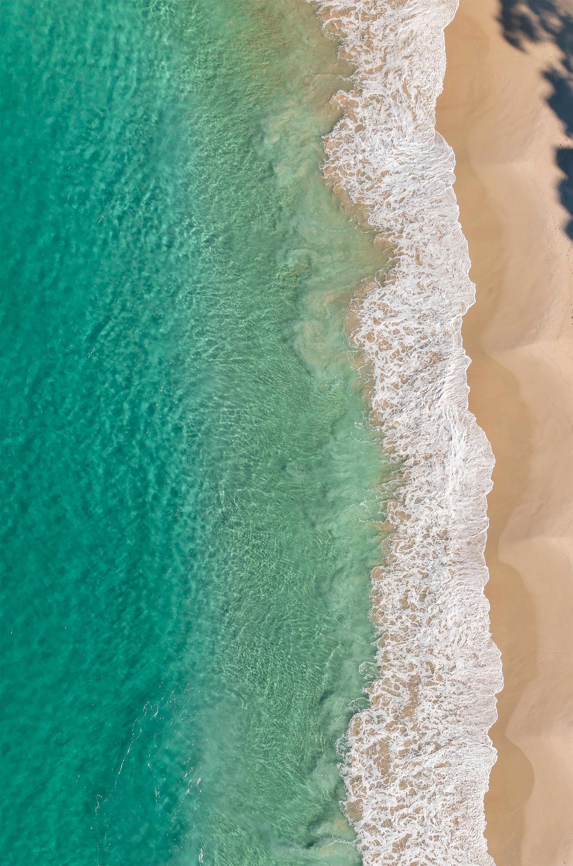 Top-down aerial of Huskisson Beach NSW, with emerald green water, white foaming wave edges and golden sand crossed by tree shadows.