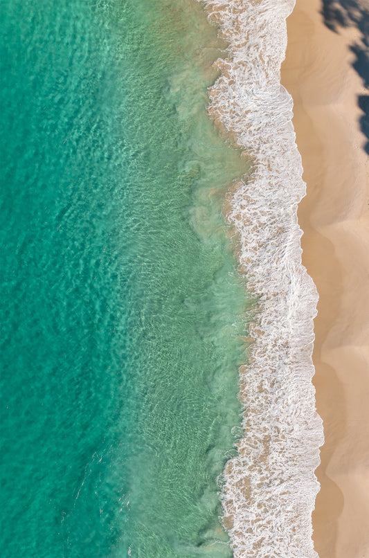 Top-down aerial of Huskisson Beach NSW, with emerald green water, white foaming wave edges and golden sand crossed by tree shadows.