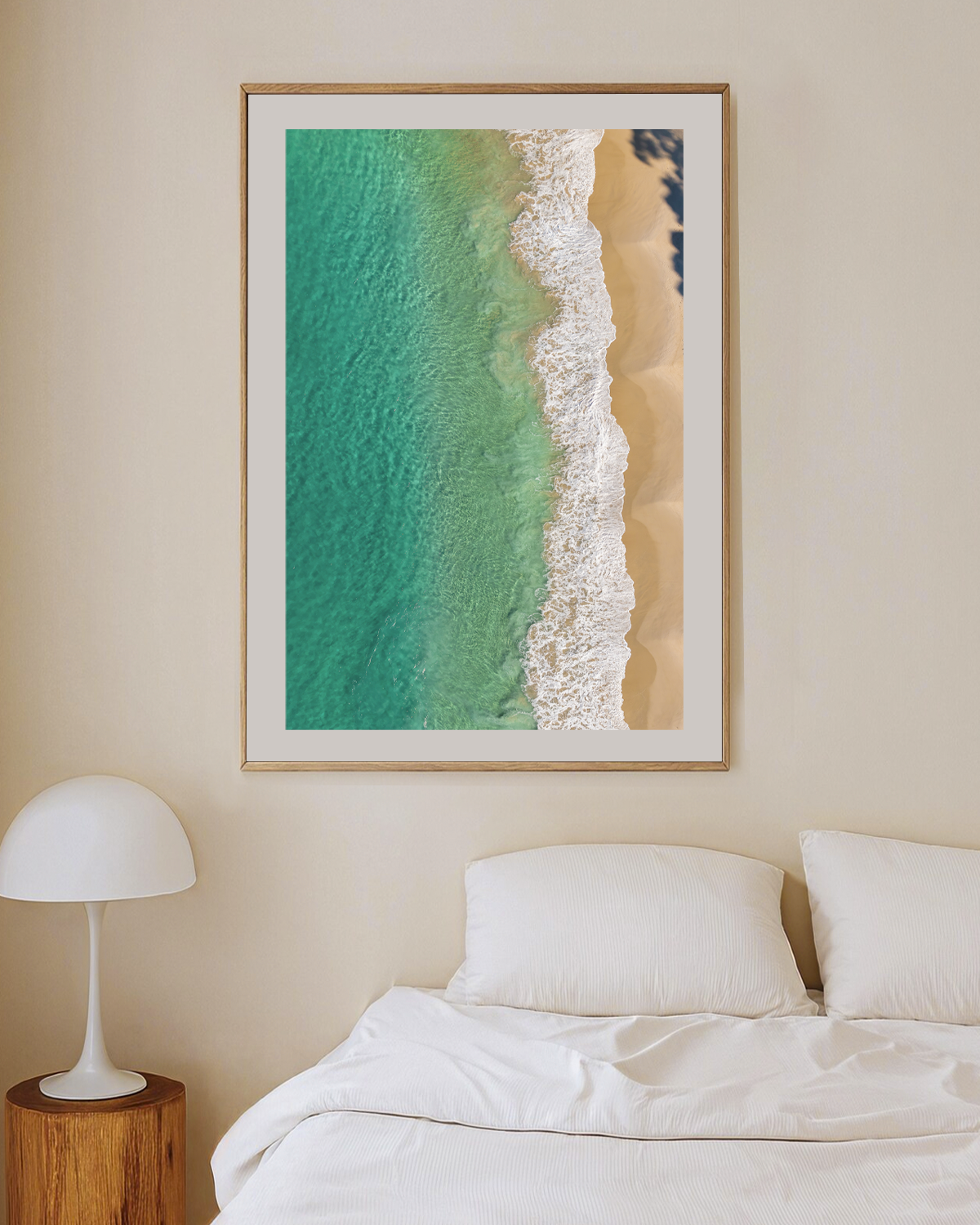 Huskisson Beach print in a natural oak frame, styled above a white bed in a soft neutral bedroom.