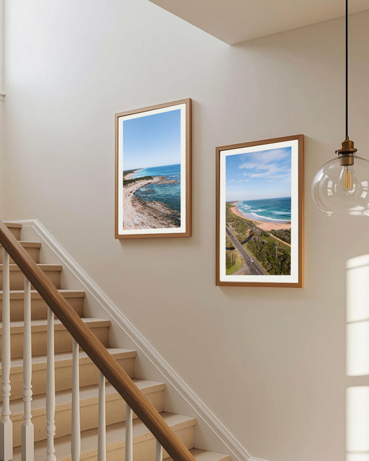 Kilcunda Trestle Bridge print in a natural oak frame, styled on a stairway wall beside another Kilcunda coastal print.
