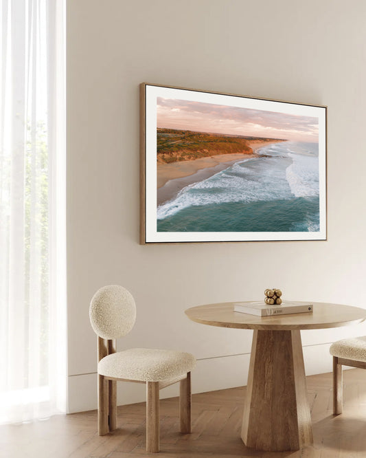 Kilcunda Sunset print in a natural oak floating frame, styled above a round timber dining table.