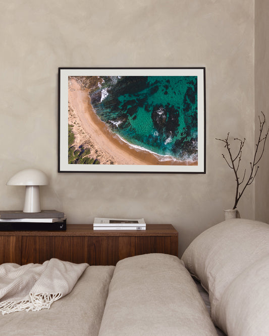 Kilcunda Beach print in a black frame, styled above a walnut sideboard beside a linen-dressed bed.