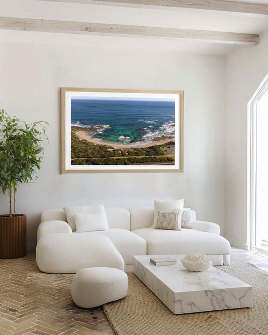 Kilcunda Cove print in a natural oak frame, styled in a white beamed living room above a boucle lounge.