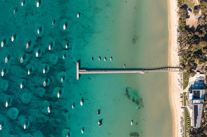Top-down aerial of the Sorrento Sailing Couta Boat Club jetty on Port Phillip Bay VIC, with couta boats and yachts moored on turquoise water.