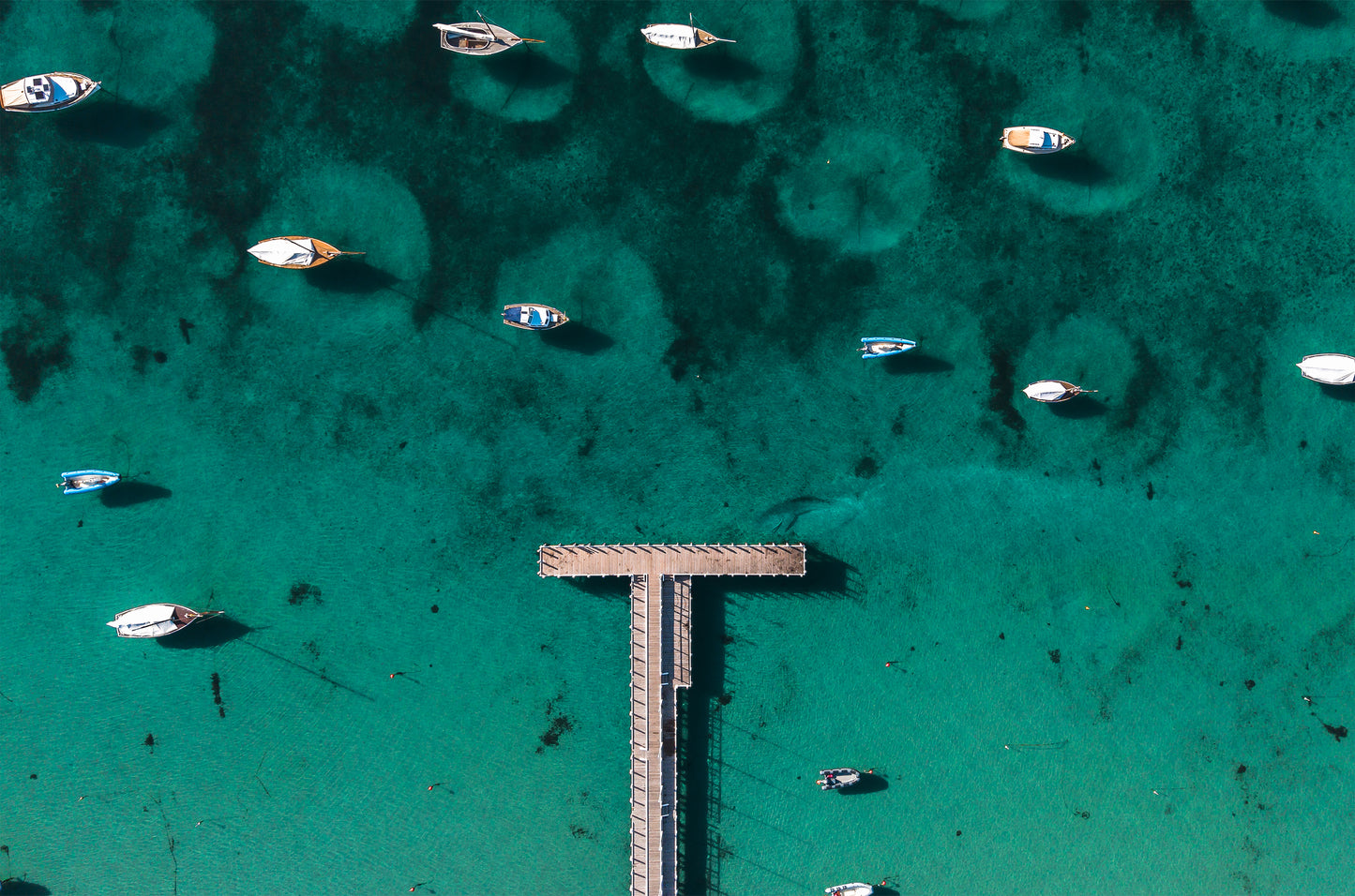 Top-down aerial of the T-shaped Sorrento sailing pier on emerald Port Phillip Bay water, surrounded by moored couta boats and dinghies.
