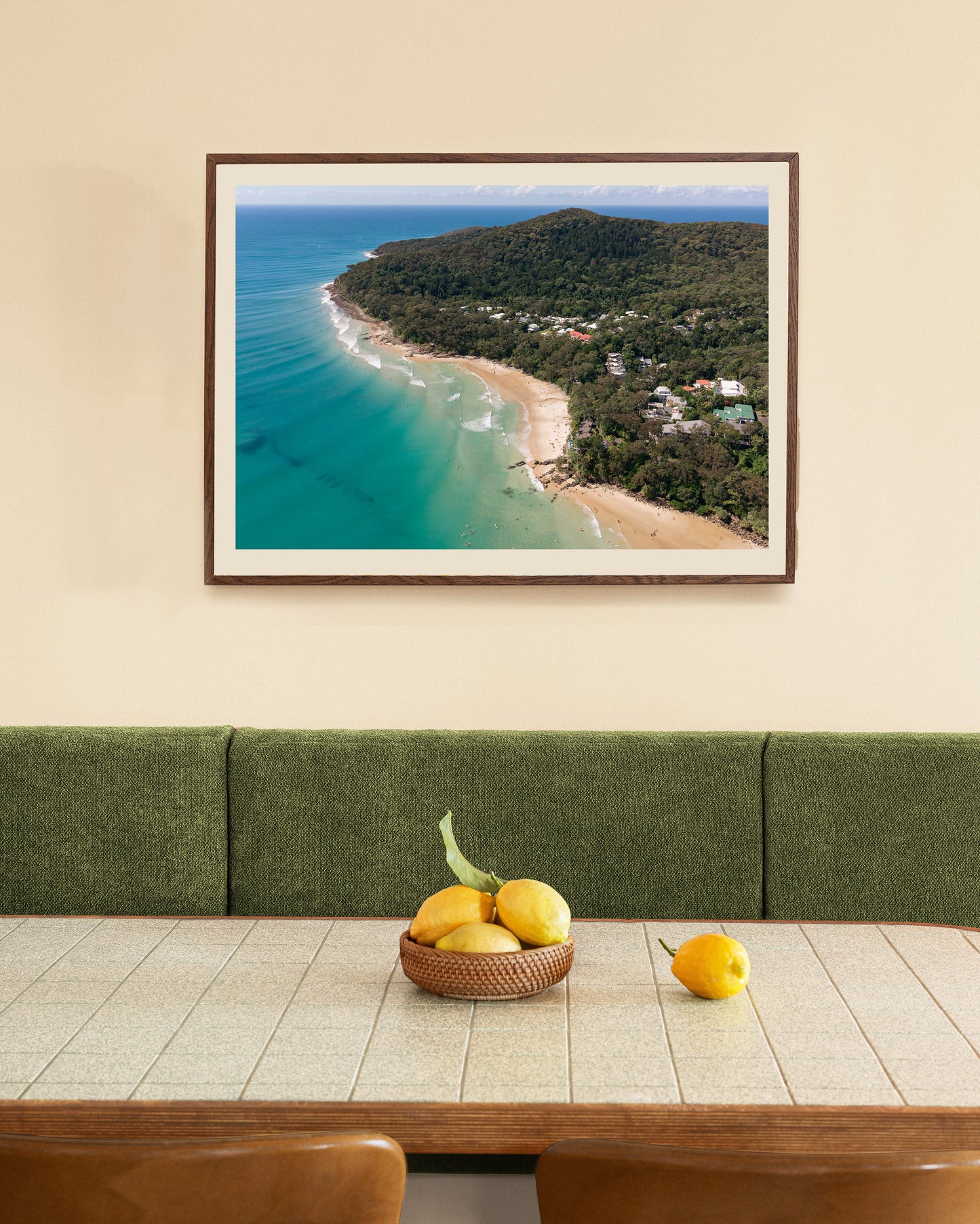 Noosa Headland and Little Cove aerial print in a natural oak frame, styled above a green velvet banquette and timber dining table.