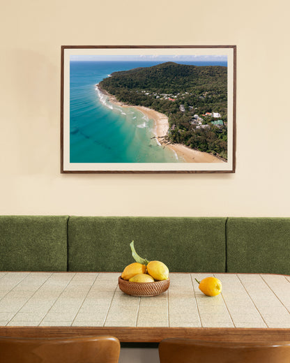 Noosa Headland and Little Cove aerial print in a natural oak frame, styled above a green velvet banquette and timber dining table.
