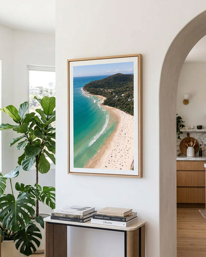 Noosa Main Beach portrait print in a natural oak frame, styled in a hallway archway beside a console table and monstera plant.
